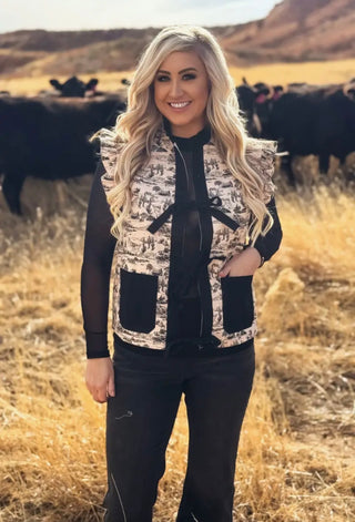 Woman standing in a field with cows wearing a western patterned vest.
