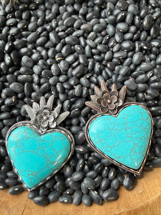 Turquoise heart-shaped brooches with floral designs on a bed of black pebbles.
